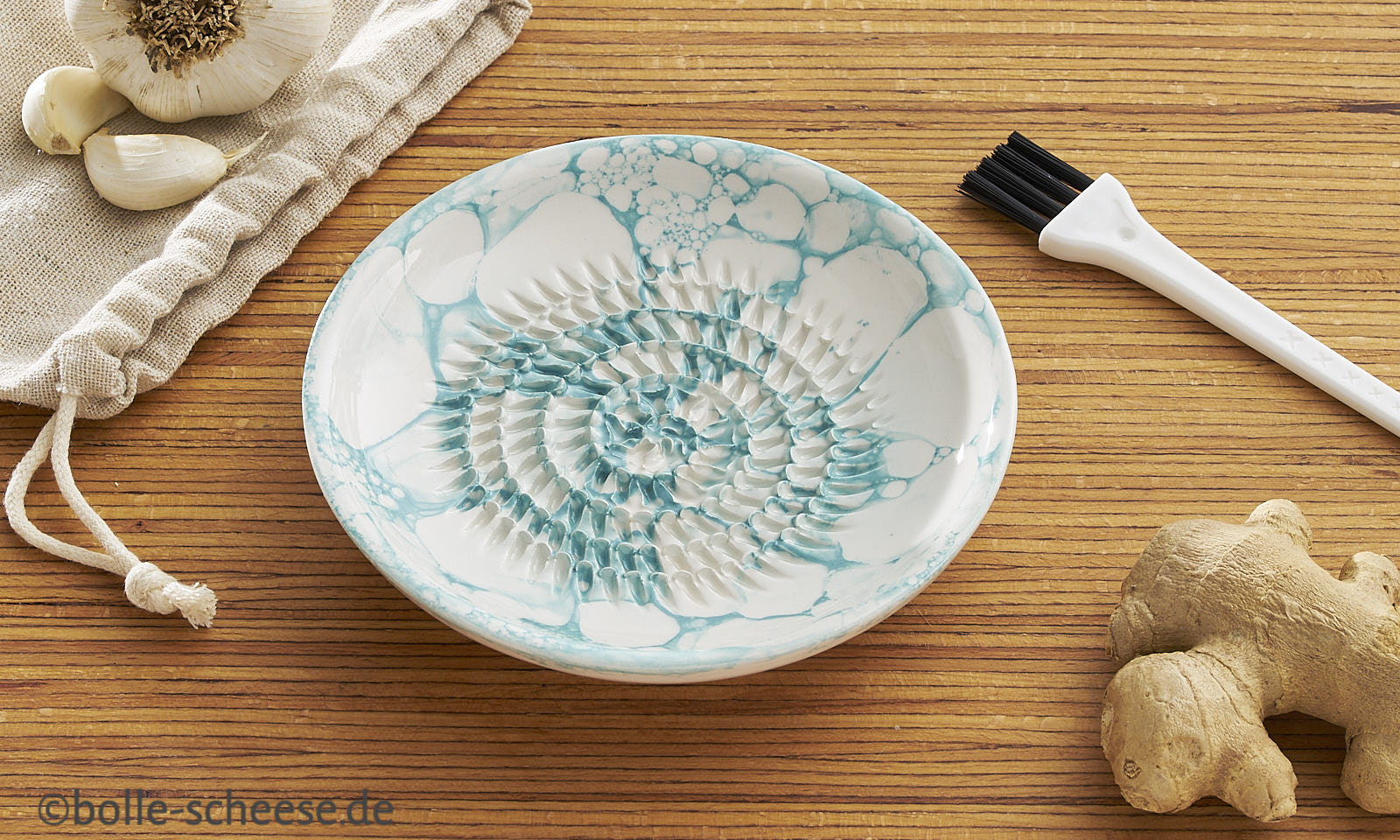 Weisse Knoblauch-Reibe aus Keramik mit tuerkisfarbenem Blasen-Muster.